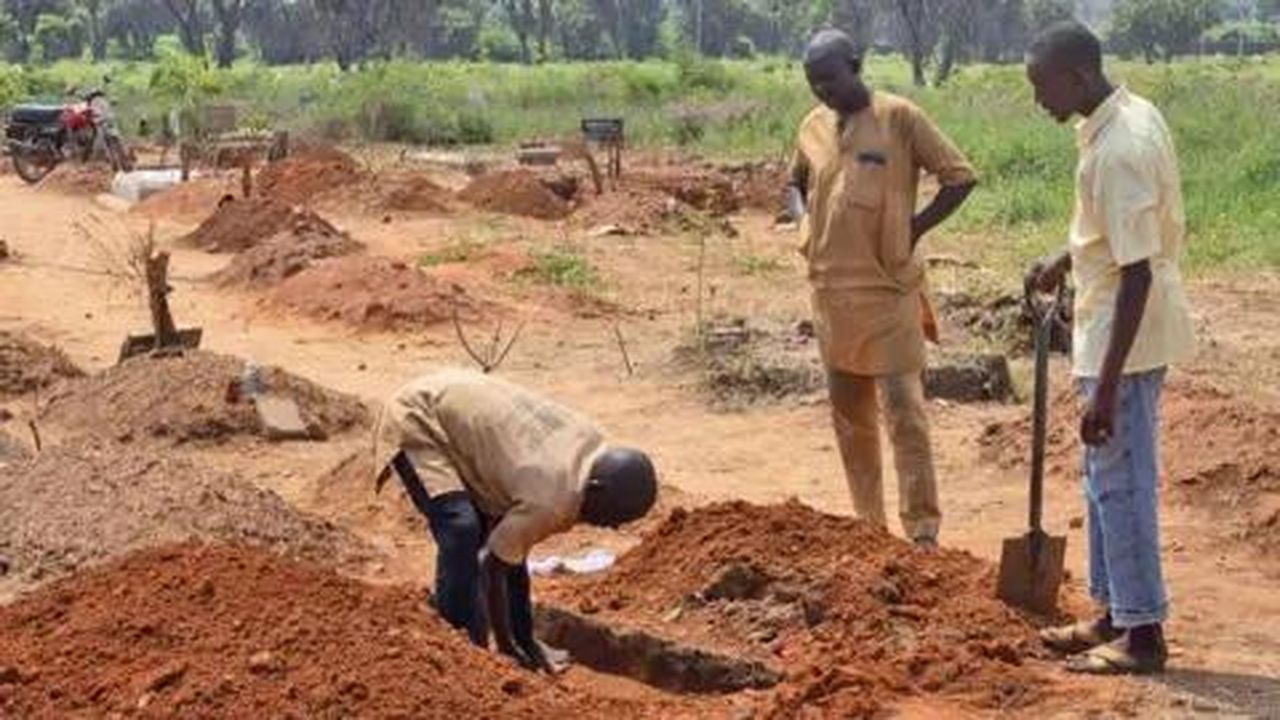 Il lavoro quotidiano al cimitero - Un uomo scava una tomba mentre altri osservano