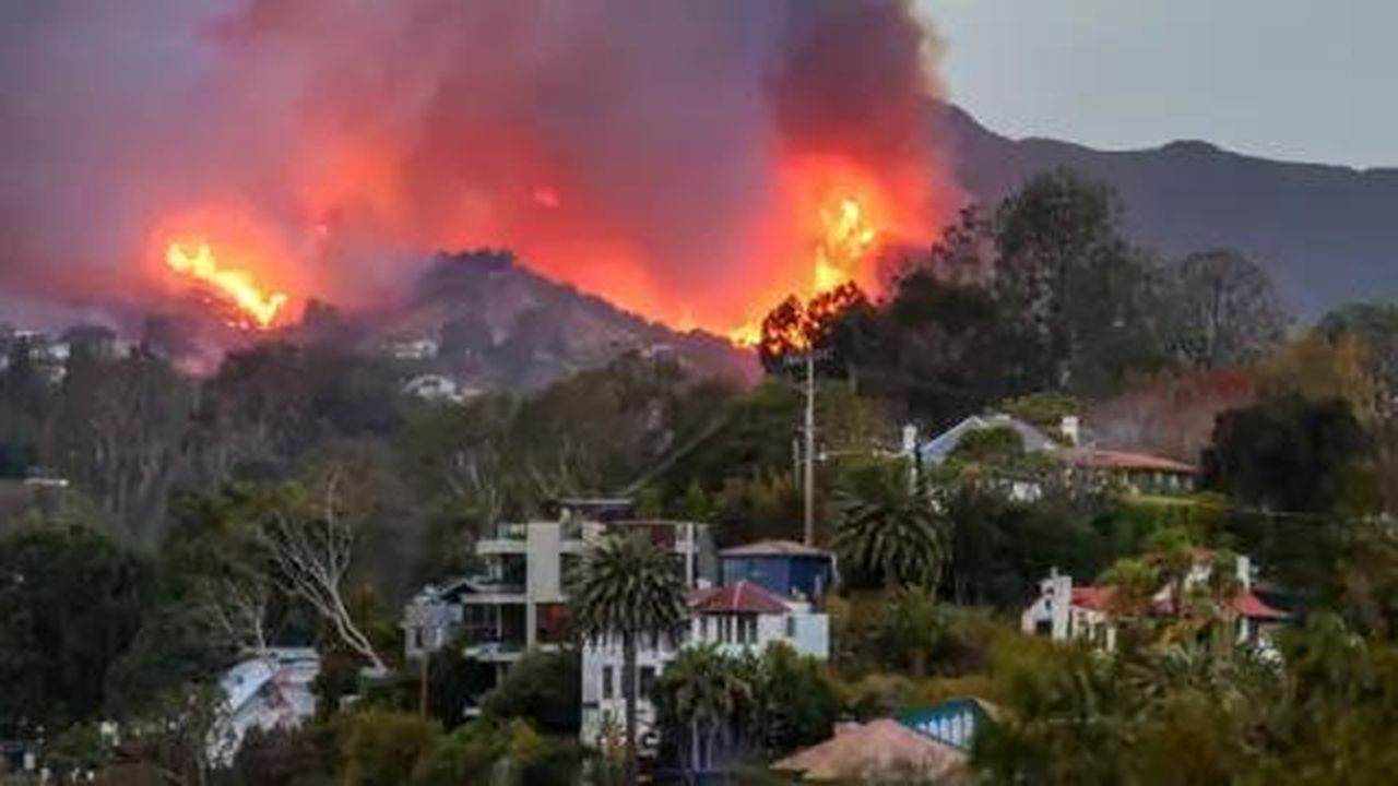 source:BBC World News - Incendio devastante a Pacific Palisades - Un incendio brucia su una collina con edifici sottostanti.